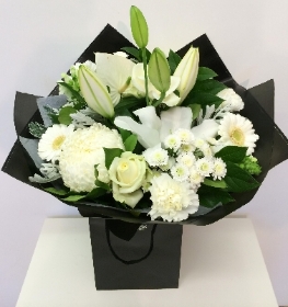 All white bold bouquet including roses, lily, and chrysanthemum with a black contrasting wrap and bag. 